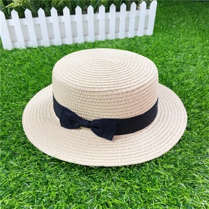 Top view of beige straw boater hat with a black bow ribbon on artificial turf