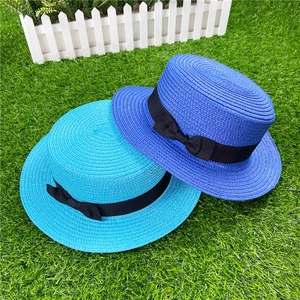 Flat top straw hat with black bow ribbon shown in bright blue and cyan on green grass