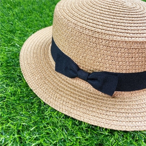 Detail of light brown straw boater hat featuring a black grosgrain ribbon and bow accent