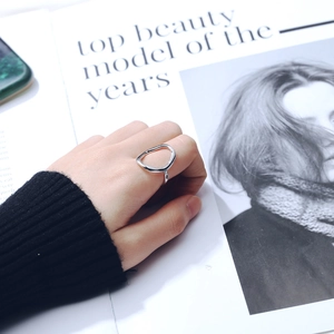 Minimalist irregular hollow geometric silver ring shown on a finger over a magazine