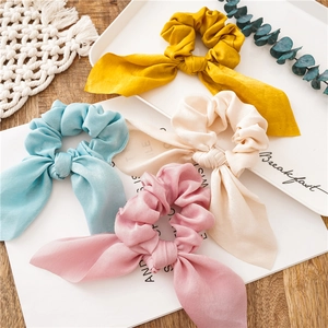 Detail of four colorful satin bow hair scrunchies in yellow, blue, cream, and pink