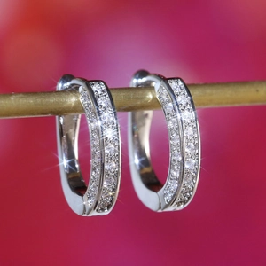 Close-up of silver U-shaped hoop earrings with micro-pave zircons on a gold rod