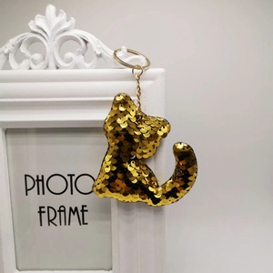 Cute golden sequin cat keychain accessory hanging on a white decorative frame