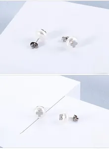 Macro detail of cross design pearl stud earrings featuring butterfly backs and silver accents
