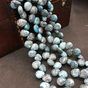 Macro view of blue-gray natural agate teardrop beads on a vintage wood box