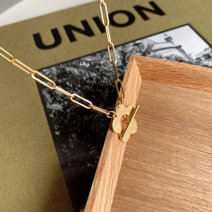 Macro shot of gold paperclip chain necklace with a floral toggle clasp on a wooden tray