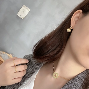 Detail shot of a minimalist gold flower toggle necklace and heart earrings on a model