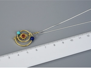 Close-up of Solar System necklace pendant showing orbits and planets against a scale
