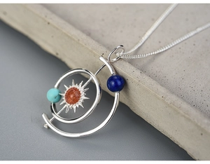 Detailed close-up of solar system pendant with orange gemstone and blue star accents