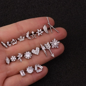 Detailed view of silver stainless steel studs and zircon piercings held on fingertips