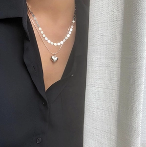 Detail of layered 925 silver heart necklace and metal disc chain worn on a black shirt