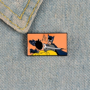 Détail en gros plan d'un pin's émaillé Batman giflant Robin sur du denim bleu clair