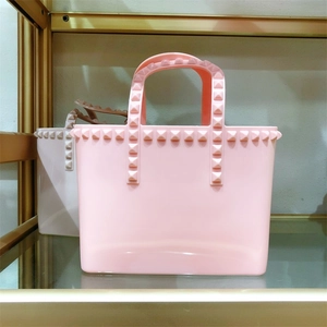 Macro shot of light pink jelly bucket bag featuring square gold rivets on the PVC handles