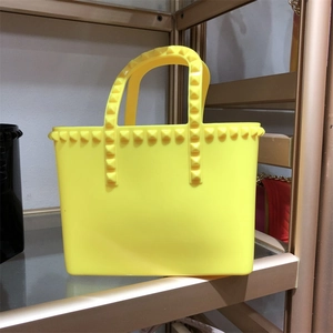 Detailed close-up of yellow jelly tote bag featuring golden pyramid stud accents