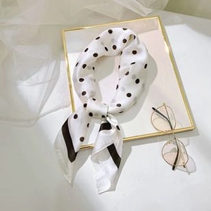 Detailed view of elegant white square scarf with black polka dots on a glass tray