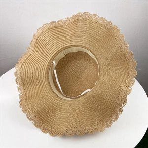 Women straw sun hat with wavy brim and elastic chin strap on a white table