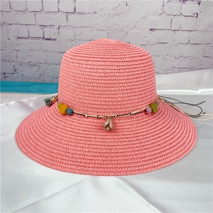 Pink straw sun hat with bohemian colorful beads and floral charms on smooth fabric background