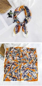 Detail view of square silk scarf with orange and blue banana leaf pattern on white fabric