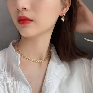 Close-up of golden leaf necklace and heart earrings on a model wearing a white shirt
