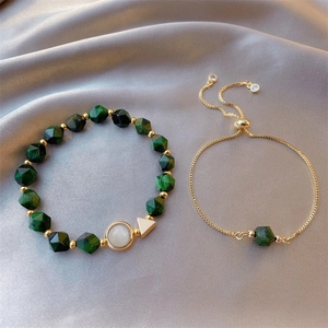 Detailed close-up of emerald green beaded bracelet set with gold chain on silk fabric