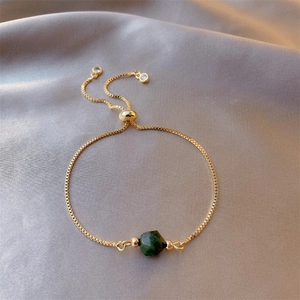 Detailed macro view of an adjustable gold emerald bracelet on elegant grey silk fabric