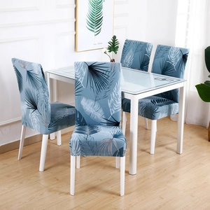 Blue stretch chair cover with tropical leaf print on four modern dining chairs in a room