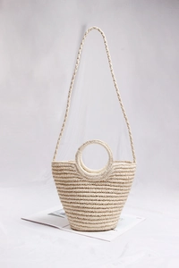 Detail of beige straw tote bag with round handle and shoulder strap on white fabric