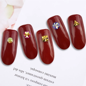Assorted metallic nail art studs and rhinestones on dark red nails with floral background
