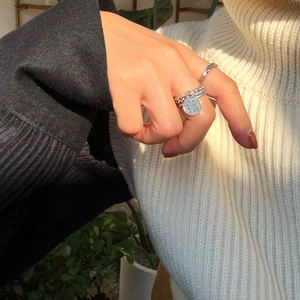 Close-up of minimalist silver chain ring set with coin pendant on a female hand