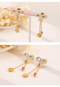 Detail of gold bow earrings with crystal tassels, snowflake and bell charms on beige background
