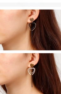 Détail de boucles d'oreilles cœur en or rose avec barres noires portées par un modèle