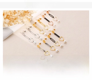 Detail of long heart-shaped earrings with drop pearls in gold and steel finishes
