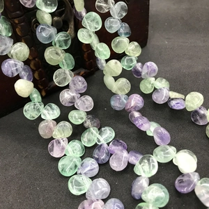 Close-up of translucent purple and green fluorite teardrop beads on a vintage wooden box