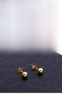 Detail of 18k gold plated solid ball stud earrings on black leather texture