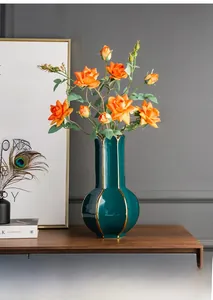 Detail of luxury green ceramic vase with gold trim and orange roses on wood cabinet