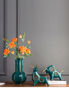 Detail of dark green ceramic vase and bull figurines with golden accents in Nordic style