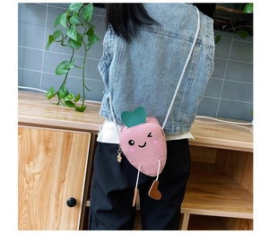 Detail showing pink carrot-shaped kids crossbody bag with green heart leaves and white strap