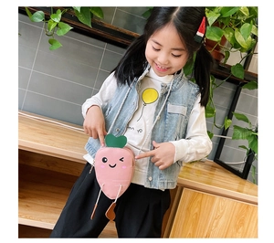 Pink carrot-shaped kids crossbody bag shown on a young girl in a natural indoor setting