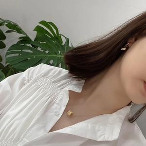 Detail of minimalist gold bead necklace and irregular earrings on a model in white shirt