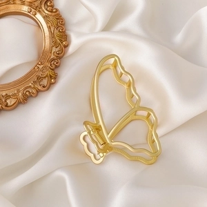 Detail of large golden matte butterfly hair claw clip on soft white silk fabric