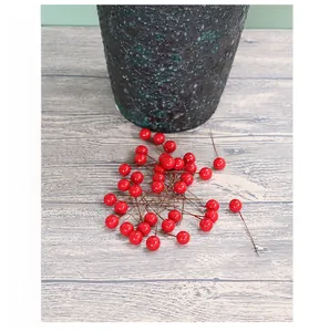 Detailed view of artificial red holly berries with brown wire stems on wooden table