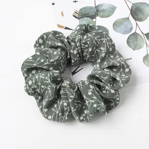 Detailed close-up of dark green floral scrunchie with white leaf pattern on white surface