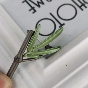 Detailed macro view of bamboo brooch featuring vibrant green leaves and textured metal stem