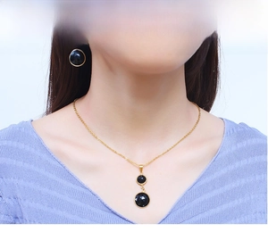Detail of model wearing a gold chain necklace and matching black round gemstone earrings