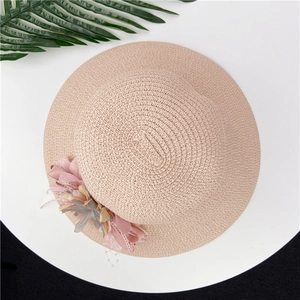 Women's foldable straw sun hat with pink chiffon flower and ribbon on white table