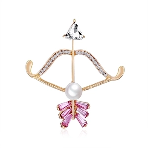 Macro shot of gold-plated crystal bow and arrow brooch with white pearl inlay