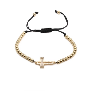 Dettaglio del bracciale con perline dorate e croce in zirconi con cordino nero regolabile