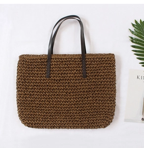Flat lay of a woven straw tote bag with brown leather handles and summer props