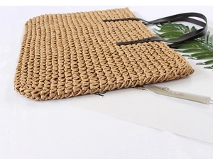 Detail of woven straw tote bag with black leather handles and tropical leaf styling