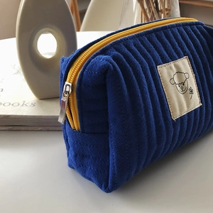 Dettaglio del beauty case in velluto blu con cerniera gialla e ricamo di un agnello